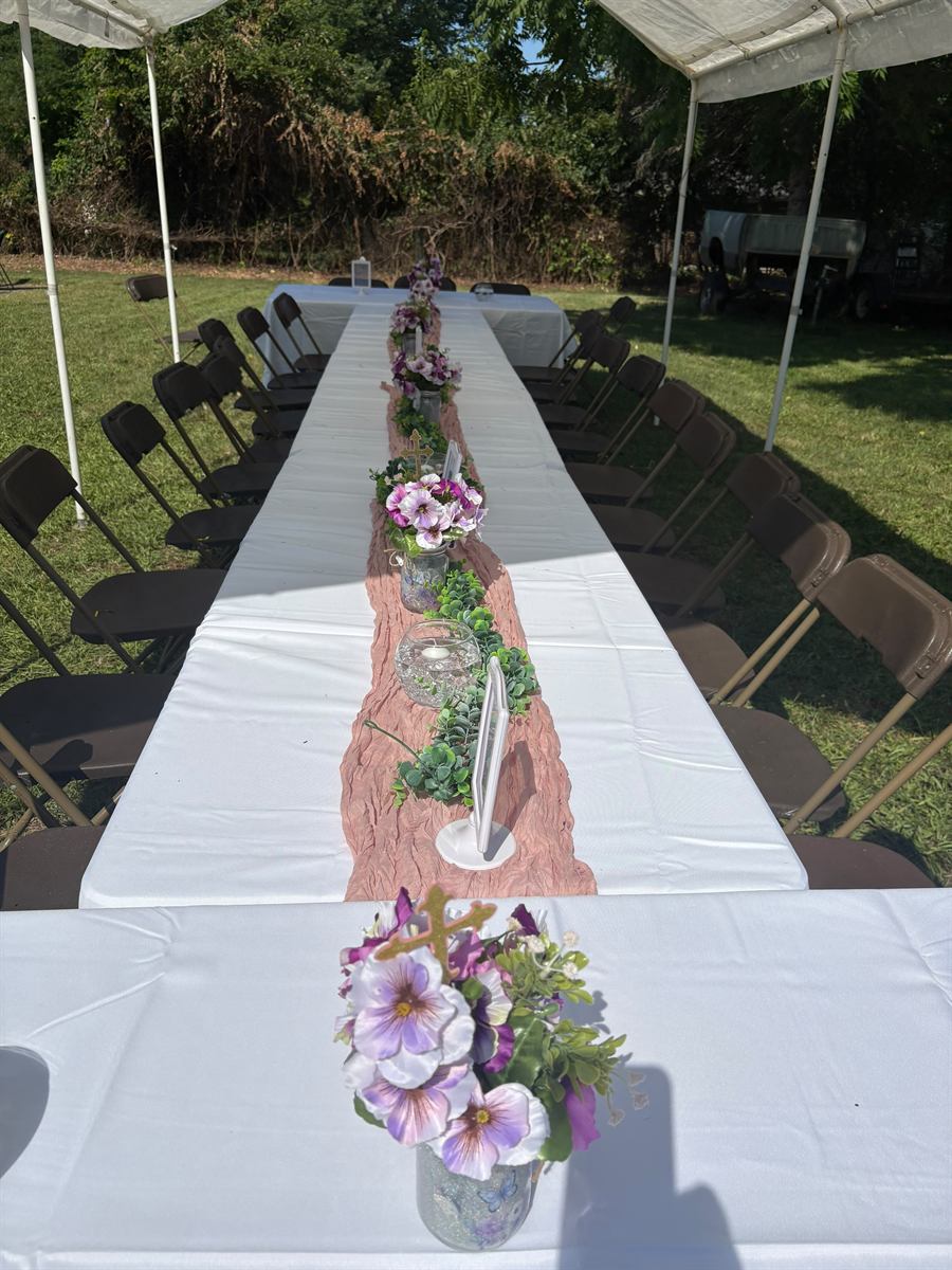 A long backyard table under a white tent with a blush runner and purple floral jars