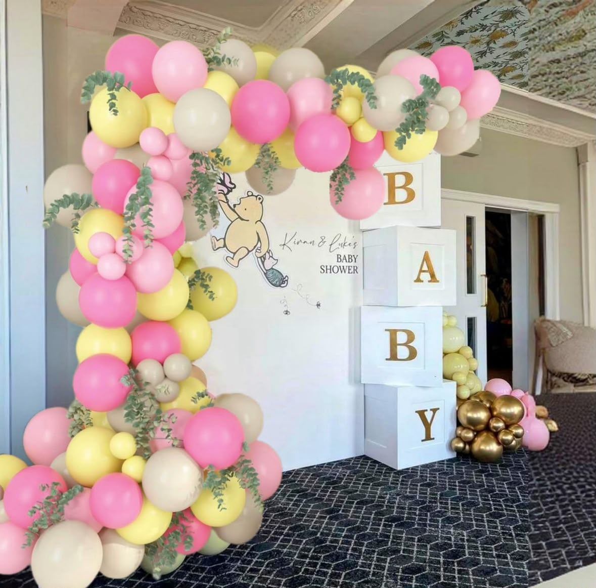 A pink, yellow and sand balloon arch framing a baby shower backdrop