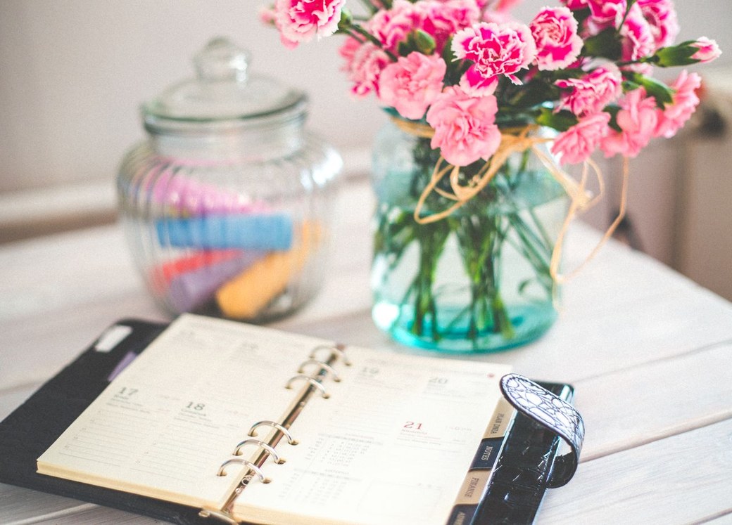 An open planner and fresh flowers on a desk during event planning