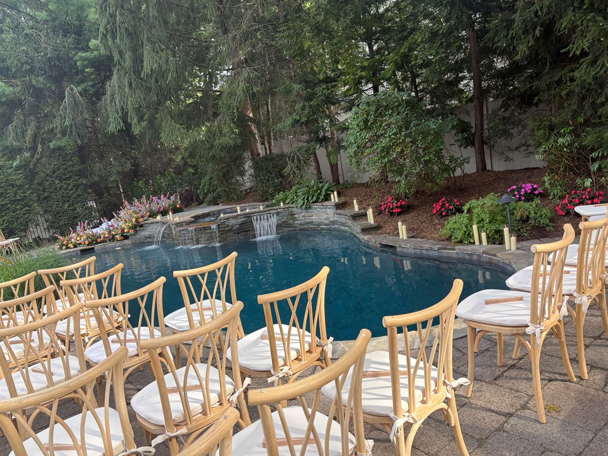 Rows of wooden crossback chairs set for a ceremony beside a candlelit pool