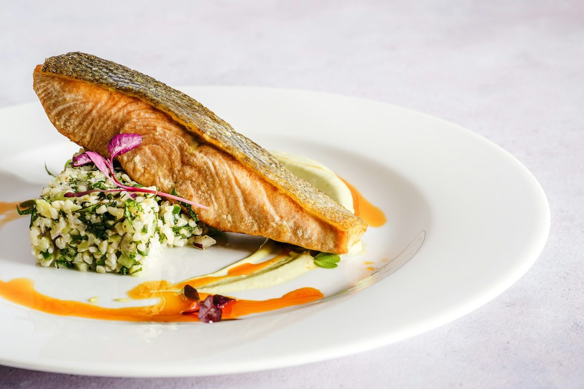A service line of plated salmon roulades on quinoa with beetroot, radish and herb oil