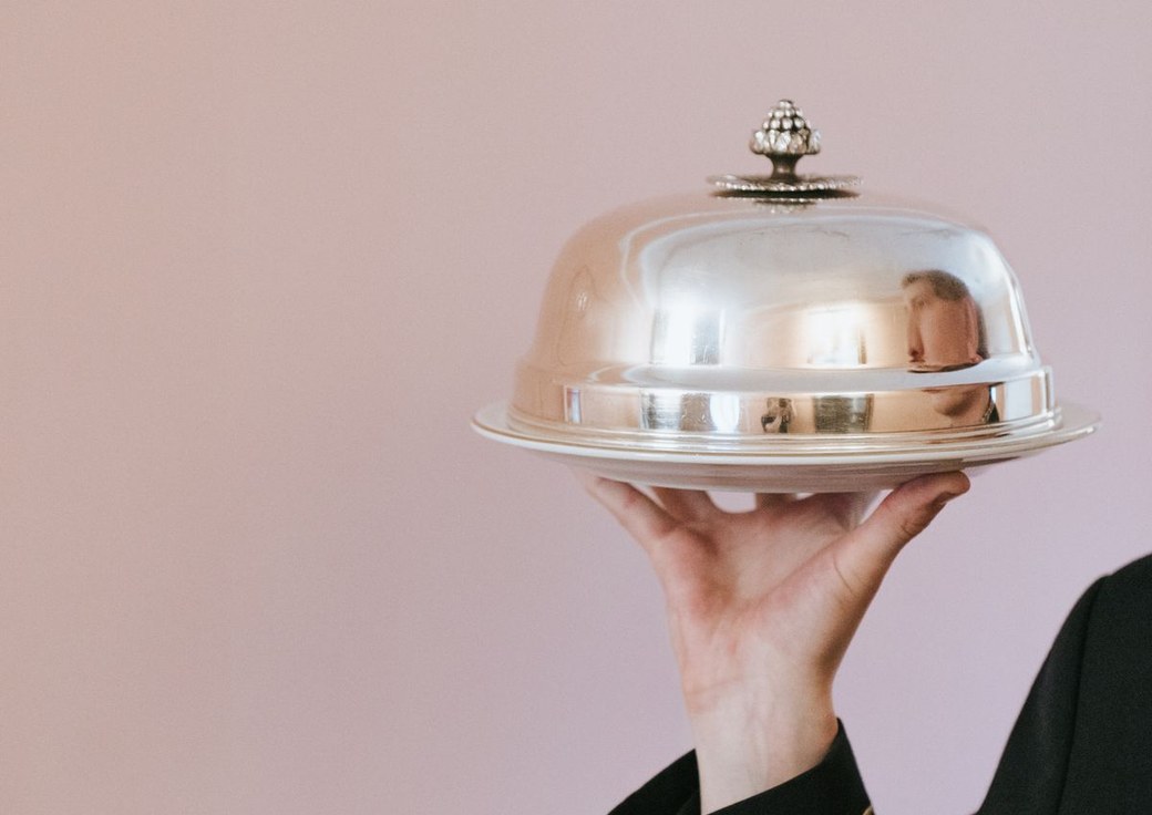 A server presenting a covered silver platter