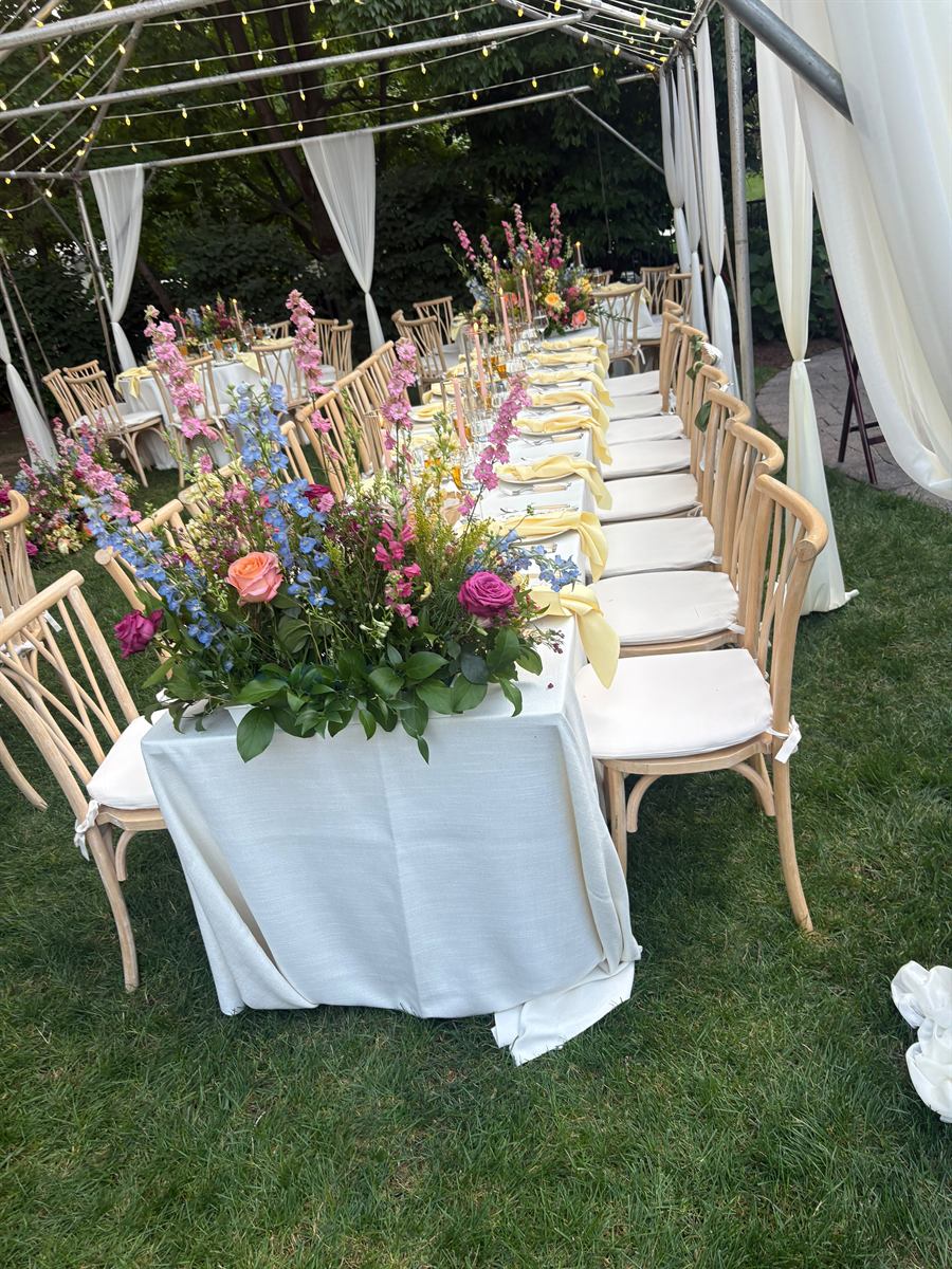 A long table under a tented marquee strung with lights, set with wildflower centrepieces at dusk